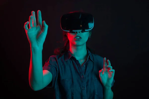 Mujer joven atractiva interactuando con alguien que usa gafas de realidad virtual en el estudio con iluminación creativa — Foto de Stock