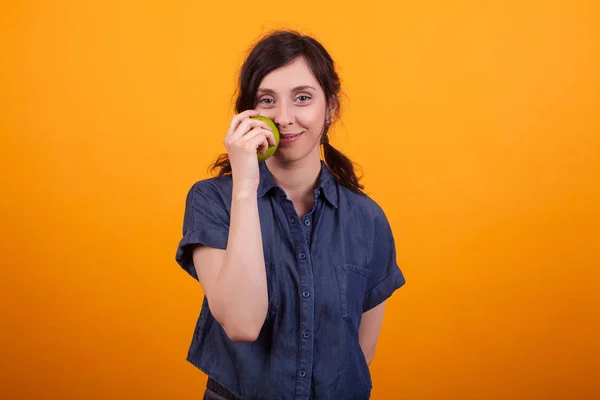 Belle femme regardant la caméra et tenant une pomme verte en studio sur fond jaune — Photo