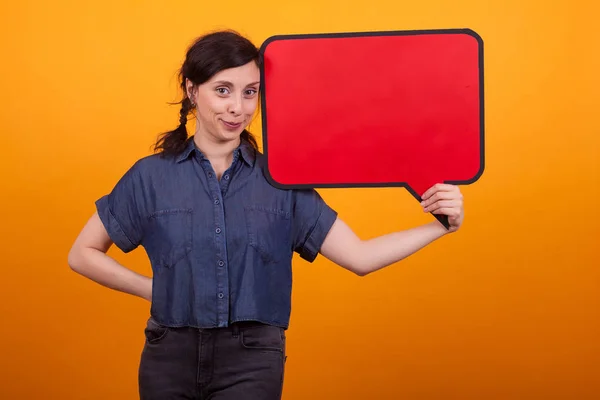 Glimlachende mooie vrouw die een lege gedachte bubbel vasthoudt en naar de camera in Studio over een gele achtergrond kijkt — Stockfoto