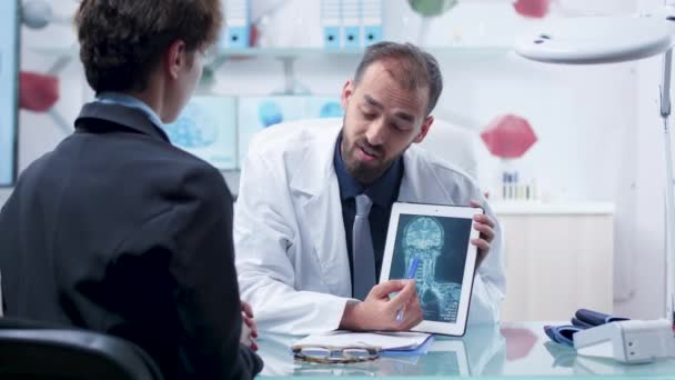 Médico en un centro de investigación moderno que muestra un escáner de rayos X en una tableta PC a un paciente — Vídeos de Stock