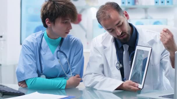 Arzt zeigt einer praktizierenden Krankenschwester ein digitales Tablet und scannt es. — Stockvideo