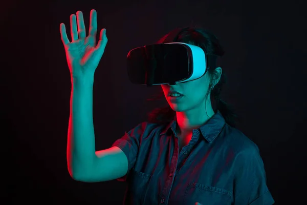 Hermosa mujer joven caucásica jugando juegos utilizando casco de realidad virtual en el estudio con iluminación creativa — Foto de Stock