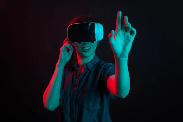 Hermosa joven sonriendo con casco de realidad virtual en estudio e iluminación colorida — Foto de Stock