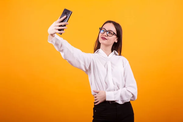 Happy jeune fille en vêtements décontractés prendre un selfie en studio sur fond jaune — Photo