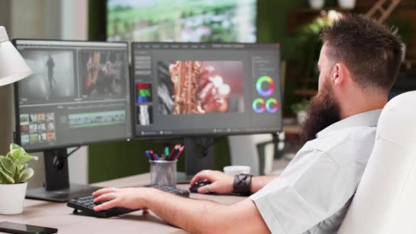 Tipo barbudo trabajar como editor de vídeo o colorista en la agencia de medios creativos — Vídeos de Stock