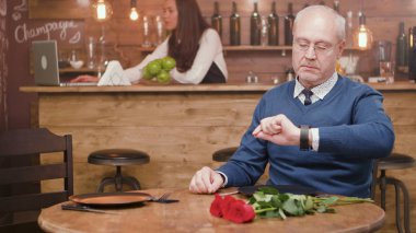 Kıdemli adam masada çiçek ile bir restoranda saatini kontrol