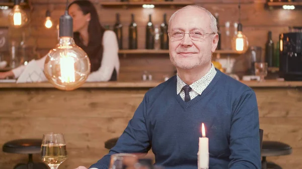 Старший чоловік за столом ресторану посміхається до камери — стокове фото