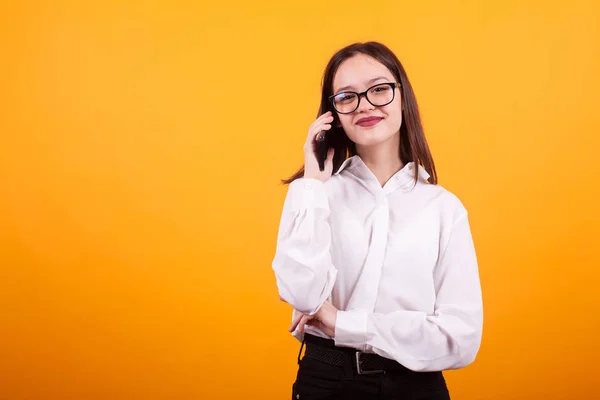 Portret van zijveren jong meisje het nemen van de telefoon en kijken naar de camera over gele achtergrond — Stockfoto