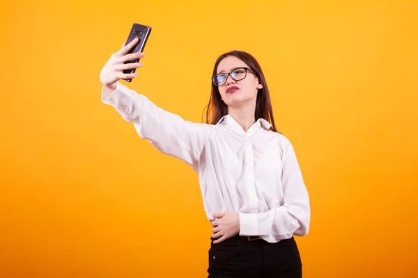 Belle jeune fille à la recherche bouleversée tout en faisant un selfie en studio sur fond jaune — Photo