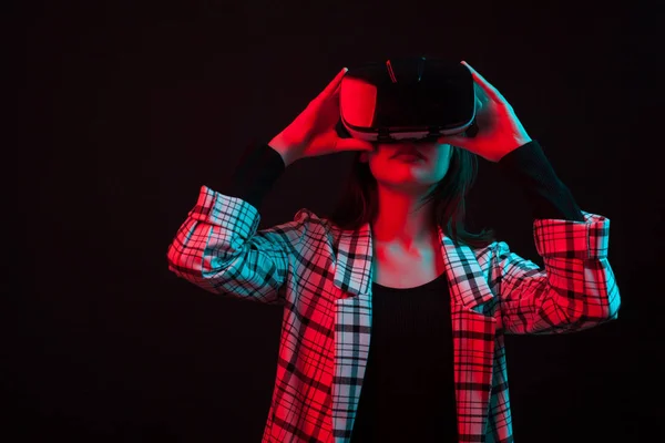 Hermosa joven utilizando la tecnología virtual moderna en el estudio sobre fondo negro con luz de color — Foto de Stock