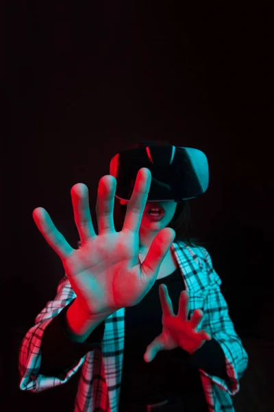 Портрет кавказской девушки в современном гаджете для виртуальной реальности в студии с цветным освещением — стоковое фото