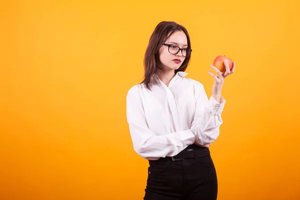 Hermosa chica adolescente caucásica sosteniendo y mirando una manzana roja en el estudio sobre fondo amarillo — Foto de Stock