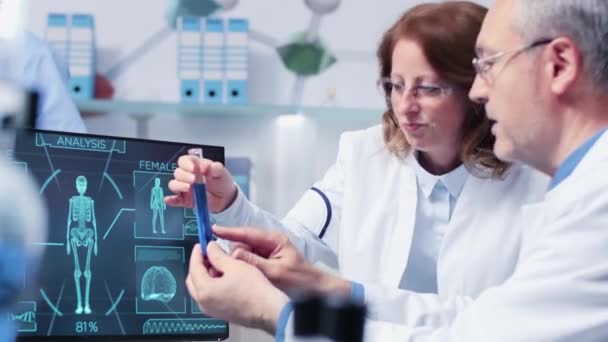 Close-up handheld footage of female and male researcher debating over a tube with blue sample — Stock Video