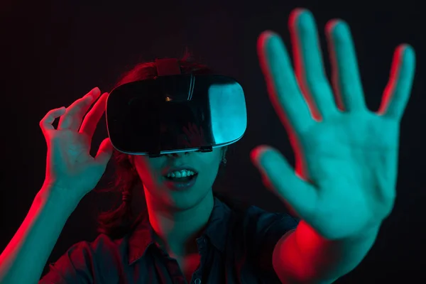 Mujer joven atractiva ajustando sus gafas de realidad virtual en el estudio con iluminación de color — Foto de Stock