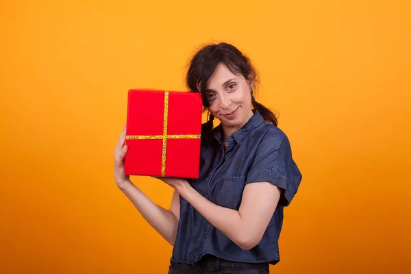 Portrait de jeune femme heureuse avec sa boîte-cadeau rouge regardant la caméra en studio sur fond jaune — Photo