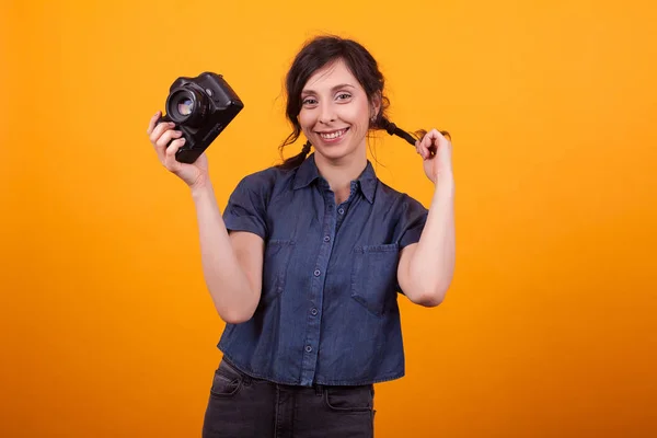 Joyeux jeune photographe avec caméra dans sa main sur fond jaune en studio — Photo