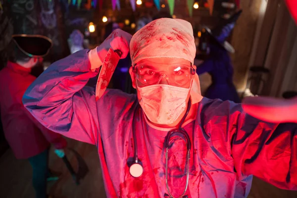 Homme tenant un couteau couvert de sang habillé comme un médecin effrayant à la fête d'Halloween — Photo