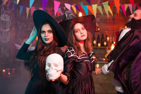 Mulheres em trajes de bruxa halloween de pé com um crânio humano na mão — Fotografia de Stock