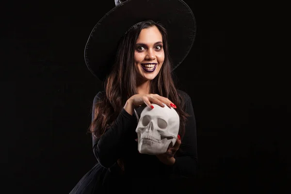 Mulher bonita vestida de bruxa para o Halloween brincando com um crânio assustador — Fotografia de Stock
