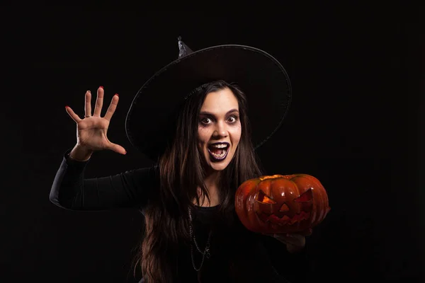 Skrämmande kvinna klädd som en häxa med en stor hatt för Halloween håller en pumpa — Stockfoto