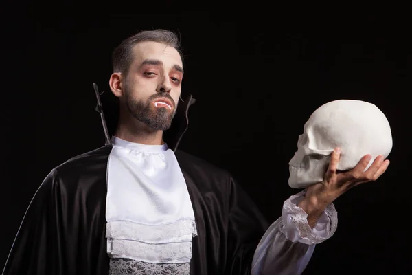 Blanc jeune homme avec effrayant visage et dracula costume regardant dans la caméra et tenant un crâne — Photo