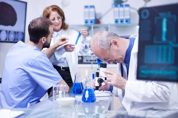 Senior scientist using a microscope in a hospital laboratory for research — Stock Photo, Image