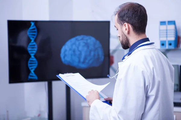Ειδικός γιατρός σε ένα εργαστήριο που κοιτάζει τη σάρωση ενός εγκεφάλου κρατώντας ένα πρόχειρο — Φωτογραφία Αρχείου