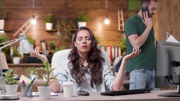 Woman meditates while her colleagues are throwing papers in the air in a very stressed work environment — Stock Video