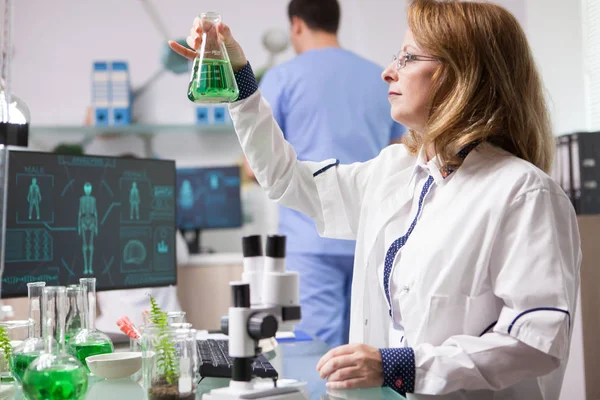 Female biologist holding and analysing a solution for healthy vegetables — Stock Photo, Image