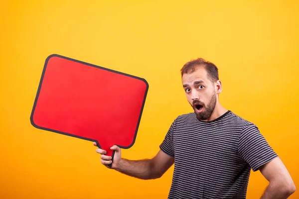 Porträt eines überraschten jungen Mannes, der in die Kamera blickt und eine Informationstafel über gelbem Hintergrund hält — Stockfoto