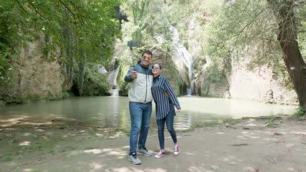 Beautiful tourist couple taking a selfie near a waterfall — Stock Video