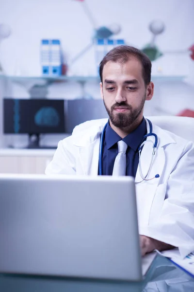 Young doctor thinking and working on his laptop in a private laboratory