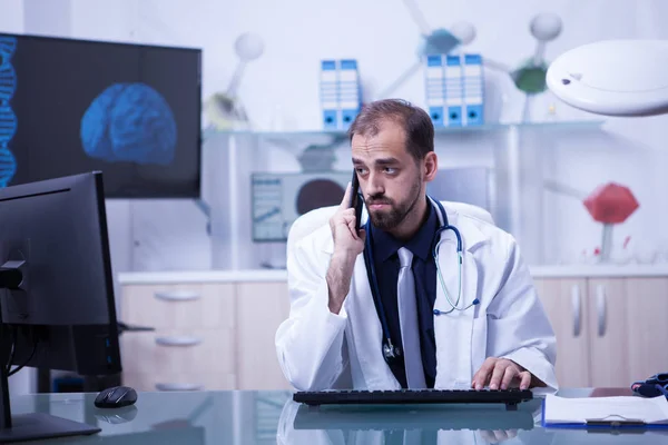 Médico varón teniendo una videoconferencia y hablando por teléfono con un paciente —  Fotos de Stock