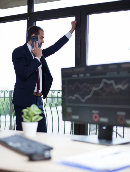 Bonito homem de negócios de terno falando ao telefone e olhando na janela de seu escritório — Fotografia de Stock