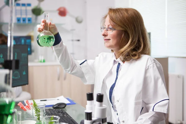 Biologa di mezza età in un laboratorio che guarda la provetta chimica — Foto Stock