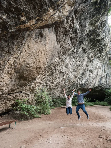 Hermosa pareja joven saltando en el aire de felicidad frente a una cueva — Foto de Stock