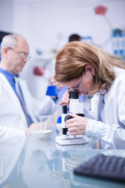 Cientista sênior fazendo pesquisa médica olhando para a amostra sob um microscópio — Fotografia de Stock