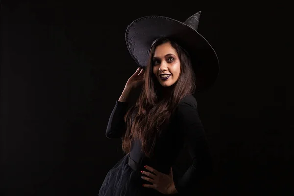 Приваблива молода жінка, одягнена як відьма на Хелловін з великим капелюхом посміхається — стокове фото
