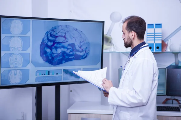 Medico con appunti sulla mano che guarda un cervello su un grande monitor — Foto Stock