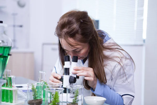 Middle age female scientist looking through a microscope in a research lab — Stock Photo, Image