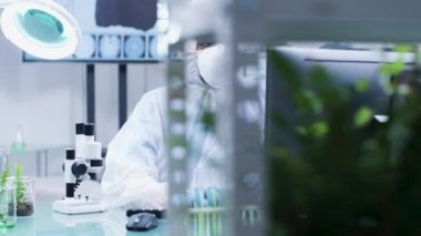 Biyolog koruyucu tulum giymiş ve maske takan bir mikroskop bakıyor