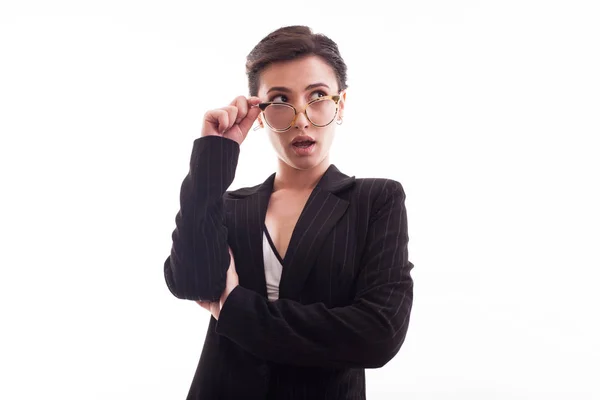 Elegante giovane modella che tiene gli occhiali e indossa una giacca nera su sfondo bianco in studio — Foto Stock