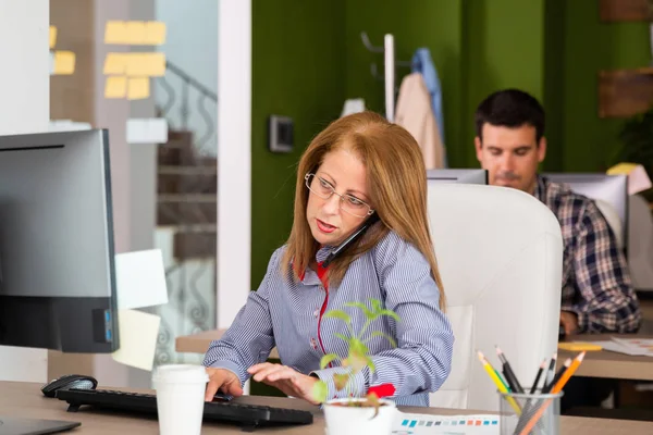 Mujer hablando por teléfono y mirando su monitor — Foto de Stock