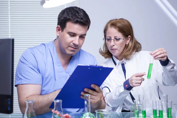 Sceintist femminile di mezza età che dice al suo giovane assistente quali appunti scrivere — Foto Stock