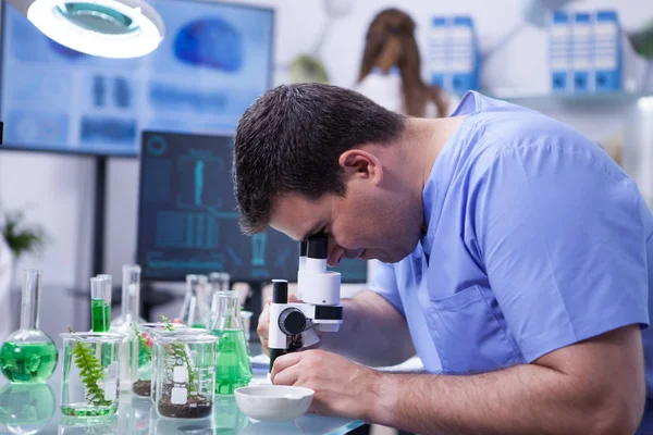 Homem cientista caucasiano em um laboratório de biotecnologia Olhando através do microscópio — Fotografia de Stock