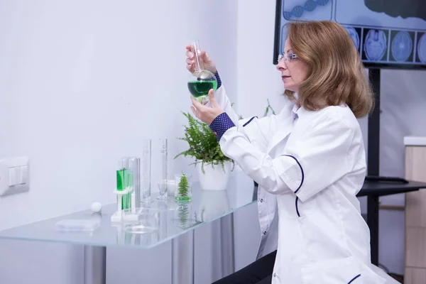 Зріла жінка-біолог дивиться на зелене рішення в її дослідницькій лабораторії — стокове фото