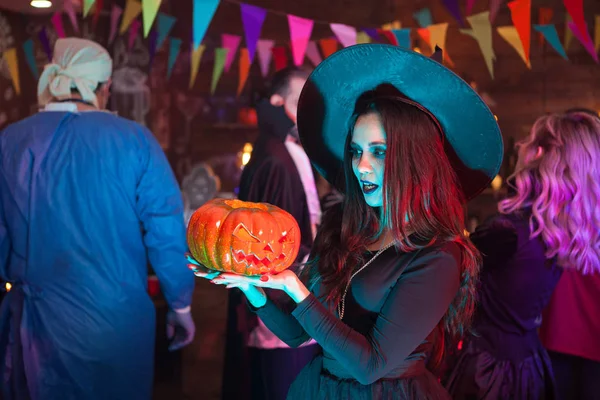 Portret van de jonge heks die geschokt op haar punmpkin voor Halloween viering — Stockfoto