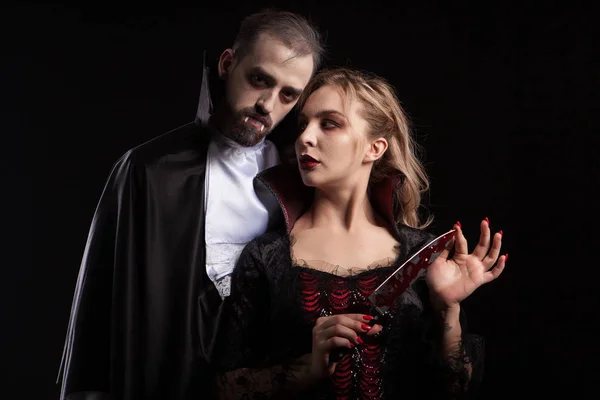 할로윈을위한 드라큘라처럼 옷을 입고 그녀의 남자를보고 혈액에 덮여 칼날과 아름다운 젊은 뱀파이어 여자 — 스톡 사진