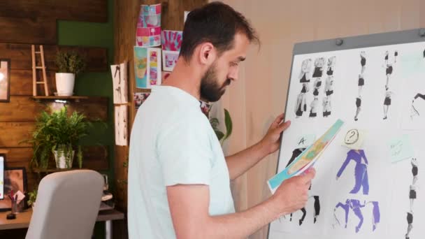 Вдумчивый молодой креативный директор проверяет дизайнерскую доску в своем творческом кабинете — стоковое видео