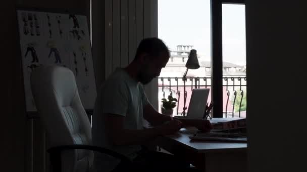 Silhoutte doświadczonego projektanta siedzi na biurku biurowego podczas pracy na komputerze — Wideo stockowe